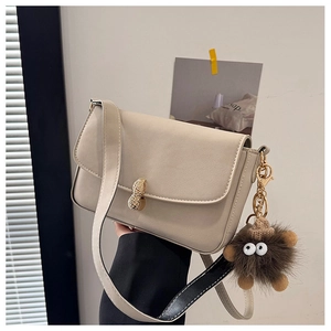 Detail of beige flap shoulder bag featuring a unique golden peanut-shaped clasp and plush charm