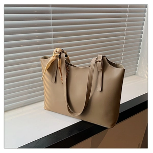 Detail of khaki leather tote bag with printed silk scarf handle on sunlit windowsill