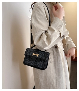 Close-up of golden H-shaped buckle on a grey and black printed leather crossbody bag