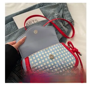 Detail of blue plaid crossbody bag featuring red trim, bow, and silver magnetic closure