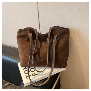 Detailed close-up of dark brown suede tote bag featuring golden leather text and white stitching
