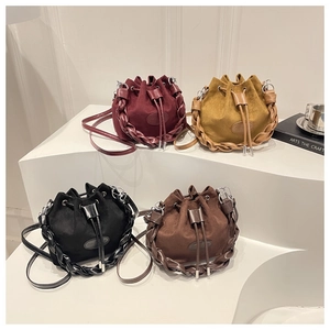 Detail of four colorful suede bucket bags with woven straps on a minimalist display stand