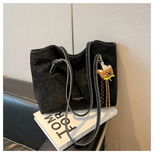Detail of black suede tote bag with contrast stitching and teddy bear charm accessory