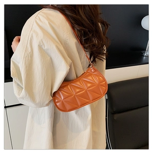Détail d'un sac à bandoulière matelassé orange porté avec une chemise beige élégante