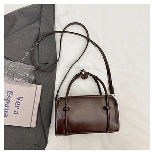 Detail of a dark brown crossbody bag with knotted handle and embossed fashion logo