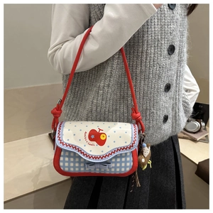 Detail of plaid crossbody bag with red trim, apple print and bear charm on shoulder