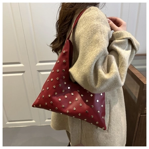 Détail d'un sac bandoulière bordeaux clouté porté par un mannequin en manteau beige