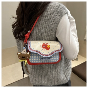 Detail of plaid crossbody bag with red apple print and a cute brown bear charm