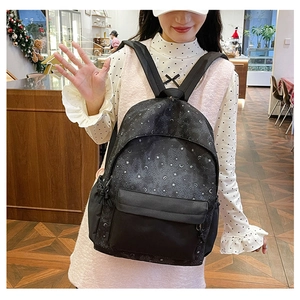 Detail of a black nylon backpack with silver star print in a cozy cafe setting
