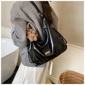Detail of glossy black hobo bag with silver logo plate and brown plush bear charm