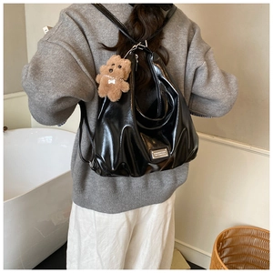 Detail of black patent leather tote bag with silver logo and cute teddy bear charm
