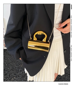 Chic cylindrical gold crossbody bag with chain strap styled on a model outfit