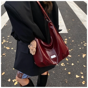 Detail of dark burgundy hobo bag with glossy finish and cute bear charm in outdoor street setting