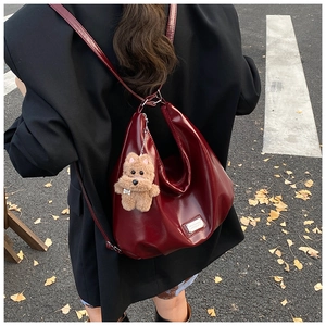 Detail of burgundy vintage tote bag with glossy leather finish and plush dog pendant charm