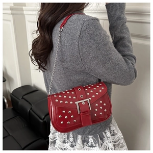 Detailed close-up of a red patent leather bag featuring punk style silver studs and buckle