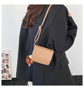 Model wearing a camel leather crossbody bag with a playful brown furry keychain charm