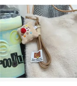 Dettaglio di ciondolo in peluche con ricamo e cinturino intrecciato su borsa di pelo