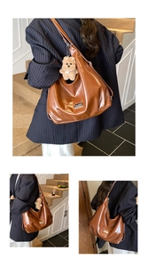 Detail of soft brown leather hobo bag with silver logo tag and plush bear accessory