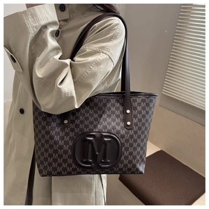 Detailed macro view of the large brown tote bag featuring embossed M letters and long leather handles