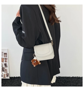 Detail of cream white faux leather crossbody bag with litchi texture and plush charm