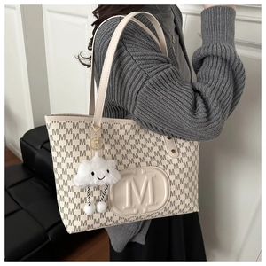 Close-up of beige tote bag with M-letter print and plush cloud charm on a shoulder