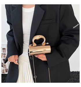 Detail of a rose gold cylindrical metallic evening bag with liquid metal handle and chain