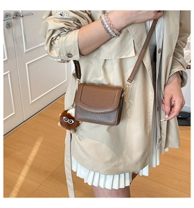 Detail of a dark brown pebble leather crossbody bag featuring a cute plush doll pendant