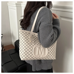 Macro detail of the embossed M letter logo and printed pattern on the beige tote bag