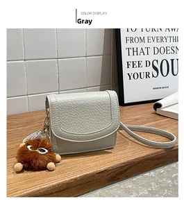 Close-up of a gray lychee pattern small square bag with a cute brown plush monster pendant