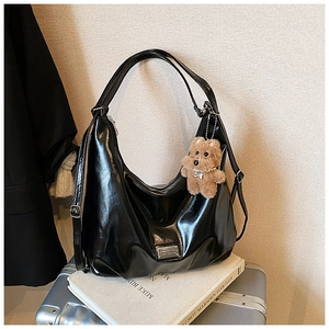 Detail of black glossy moon hobo bag with teddy bear charm on metal suitcase