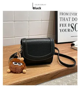 Close-up of black litchi leather crossbody bag with brown plush pendant and sunglasses