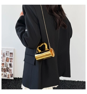 Detail view of a gold cylindrical bag with a unique handle and fine metal chain strap