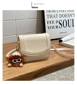 Close-up of cream white lychee pattern leather mini crossbody bag with cute brown plush charm