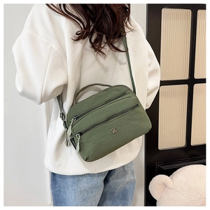 Detail of olive green nylon crossbody bag with three zipper compartments and adjustable strap