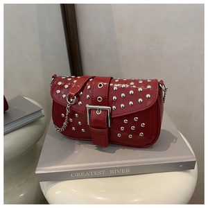Close-up of red patent leather shoulder bag with silver studs and metal buckle detail