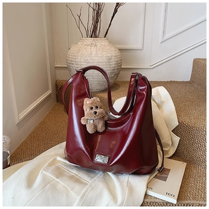Detail of burgundy tote bag with glossy faux leather texture and plush bear charm