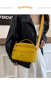 Detail of bright yellow nylon crossbody bag featuring multi-zipper layers and wide strap
