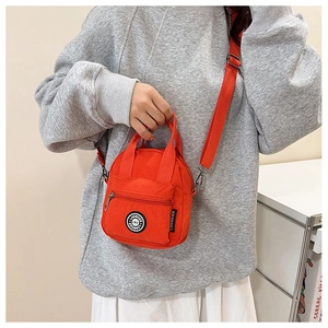 Detail of vibrant orange nylon handbag with adjustable strap and circular logo emblem