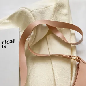 Detailansicht des rosa Leder-Schultergurts mit Goldschnalle auf Tweed-Stoffhintergrund
