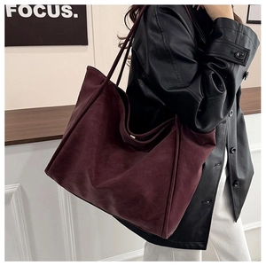 Detailed view of a large burgundy tote bag in matte synthetic leather on a shoulder