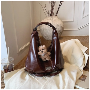 Detail of dark brown glossy hobo bag featuring a metal logo plate and plush bear charm