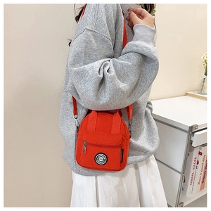 Detail view of vibrant orange nylon crossbody bag with dual handles and front zipper pocket