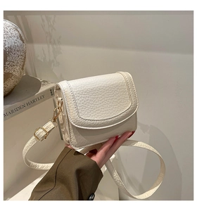 Close-up of beige pebble grain leather crossbody bag with elegant gold hardware