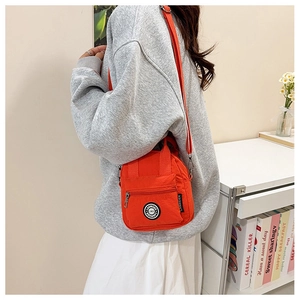 Detail of orange nylon crossbody bag featuring front zipper pocket and adjustable strap