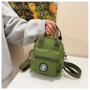 Detail view of green nylon mini crossbody bag featuring a front zipper pocket and round badge