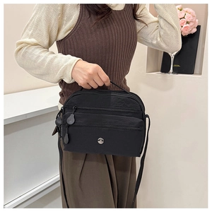 Detail of a black multi-zip crossbody bag with silver logo on a casual model outfit