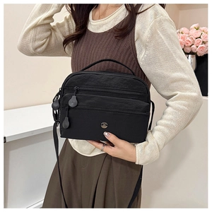 Detail view of black multi-layer nylon crossbody bag with zipper pockets and logo