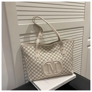 Detail view of large beige tote bag featuring embossed M logo and stylish letter print