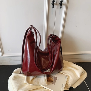 Minimalist wine red leather tote bag with wide strap and silver plate on white backdrop