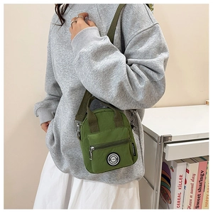 Detail of green nylon crossbody bag showing the round brand logo and canvas texture